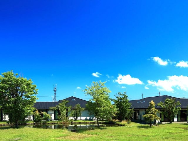 緑に囲まれた外観 外観   広い芝生と池のある敷地に、落ち着いた色合いの建物が建っています。青空の下で、のびのびとした環境が伝わります。