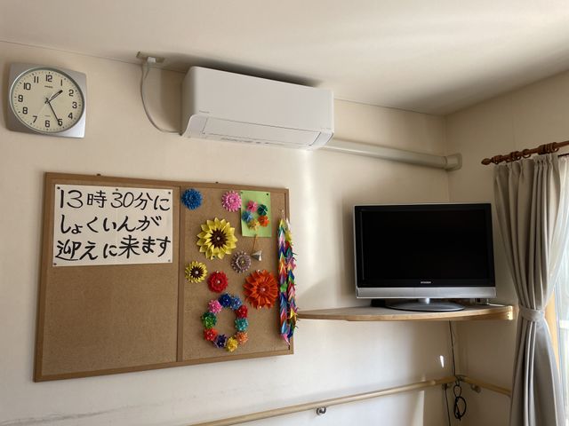 居室の壁面装飾 居室 掛け時計とテレビが設置された居室で、壁にはカラフルな手作りの装飾が飾られ、温かみのある雰囲気です。