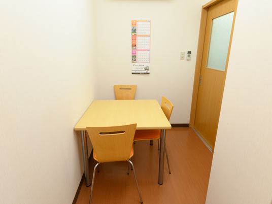 施設の写真 相談室は個室になっている。椅子がセットされた３人掛けテーブルが置かれており、壁にカレンダーが貼られている。