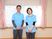 サムネイル 施設の写真 水色のポロシャツを着た男女２人のスタッフが窓の前に並んで立っている。背後の壁には、手すりが設置されている。