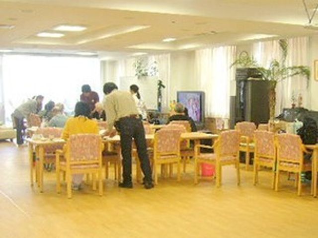 明るい共有ダイニングルーム 食堂 広々としたダイニングルームでは、スタッフが利用者さまのお世話をされており、コミュニケーションも活発です。明るく開放感のある空間で食事や会話をお楽しみいただけます。