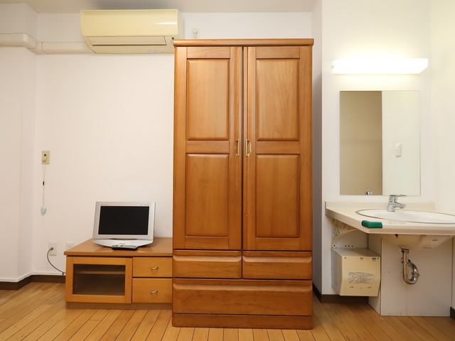居室内の洋服箪笥と洗面台 クローゼット 快適な個室での勤務が考えられ、洗面台や収納スペースも整っています。机にはパソコンも置かれ、仕事の準備も行えます。