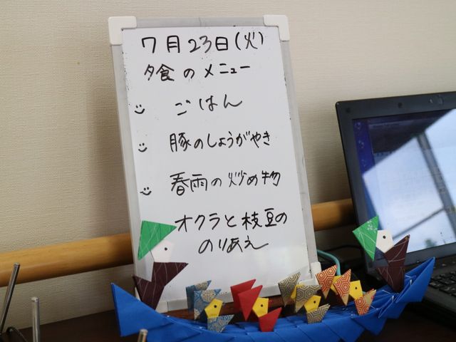 掲示物と手作り折り紙 献立表 毎日のメニューや予定が書かれた掲示板と色とりどりの手作り折り紙があります。日常の小さな情報や彩りが、快適な就業環境を形作っています。