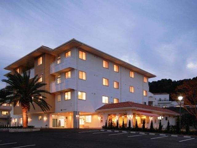 夕方の建物外観 外観 広々とした駐車場が完備されており、訪れる方に便利です。建物は温かみのある照明で包まれています。