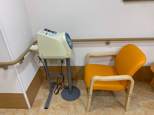 足元ケア機器のある廊下 廊下   手すりのある明るい廊下に、足元ケア用の機器と椅子が置かれています。移動しやすさと休憩のしやすさが感じられる空間です。