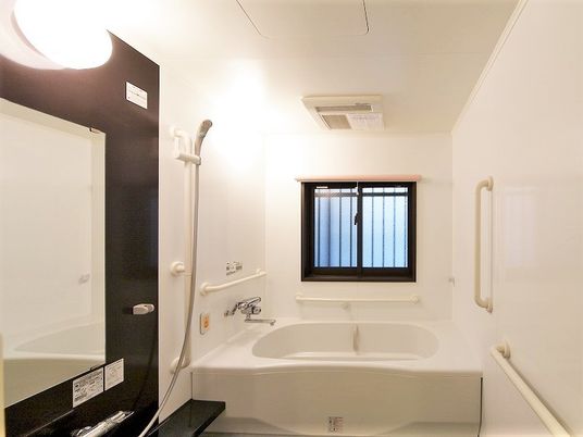 施設の写真 白い浴槽が置かれた広い浴室。大きな鏡が付いたシャワーや手すりも設置されている。