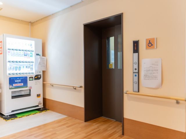 廊下と自動販売機 内観 手すり付きの廊下に隣接するエレベーターは、ご利用者様の移動をサポートします。自動販売機も備え、小さな休憩もできる工夫がされています。