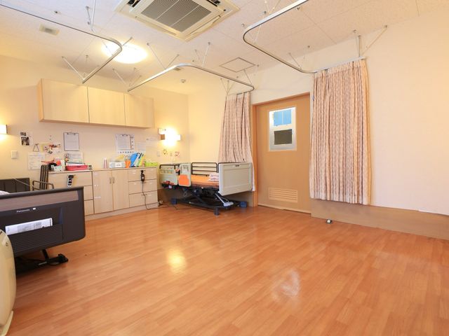 快適な居室の一角 居室 広々とした居室には、清潔感のあるベッドと多機能キャビネットが備わり、日々の生活に必要な機能が整っています。明るい窓辺のカーテンが心地よい空間を演出しており、安らぎある時間を過ごせそうです。