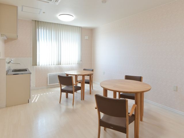 明るい居室の空間 内観 ゆったりとした居室は、明るく温かみのある壁紙と木製家具で落ち着いた雰囲気を醸し出しています。キッチンスペースもあり、自由な生活をサポートします。