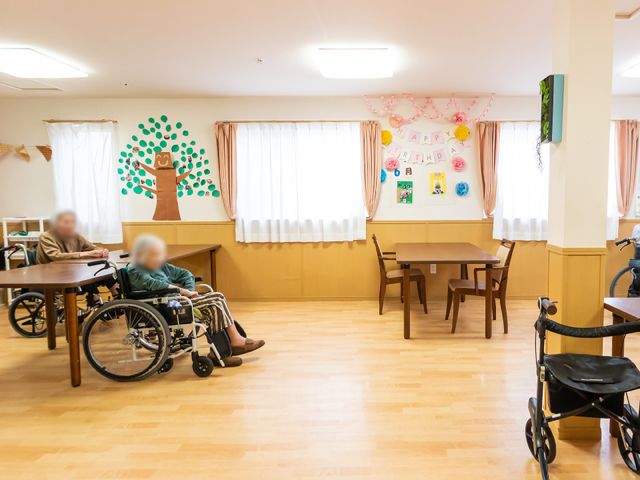 多目的室の明るい空間 共有スペース 木の温もりを感じる多目的室で、利用者の方々がゆったりとした時間を過ごされています。壁には季節感ある飾り付けが施され、暖かな雰囲気を醸し出しています。