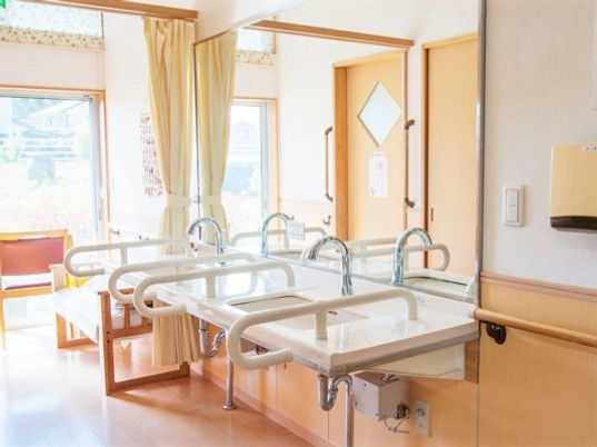 手すり付きの洗面所が二つ並び、その横にはベンチが置かれている。大きな窓からは明るい陽の光が降り注いでいる。
