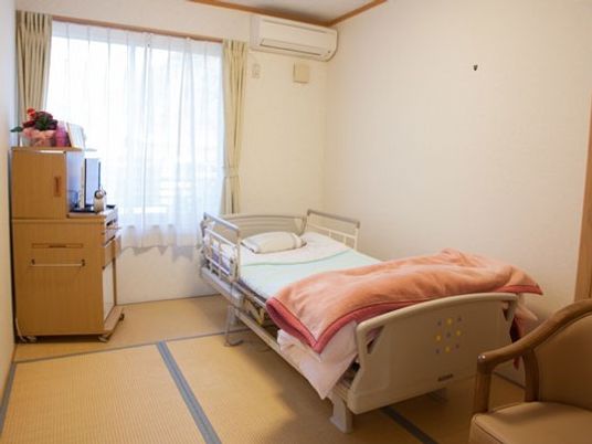 畳敷きの和室にはエアコンやカーテン付きの窓があり、寝具付きのベッドやテレビが置かれている。