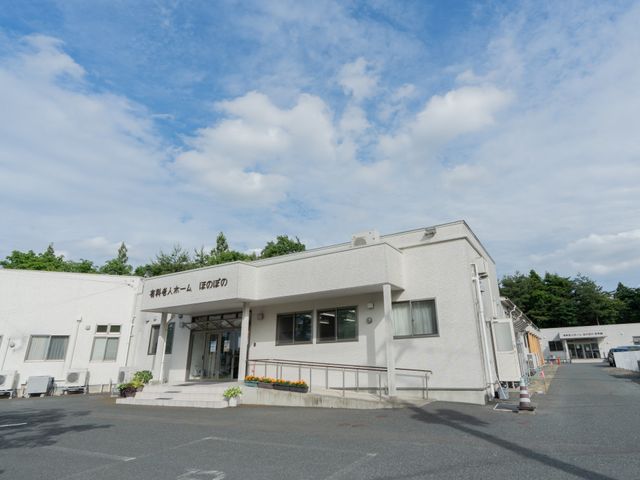入り口のある建物の外観 外観 広々とした敷地を持つ施設の外観です。青空の下、緑に囲まれた落ち着いた環境が感じられます。