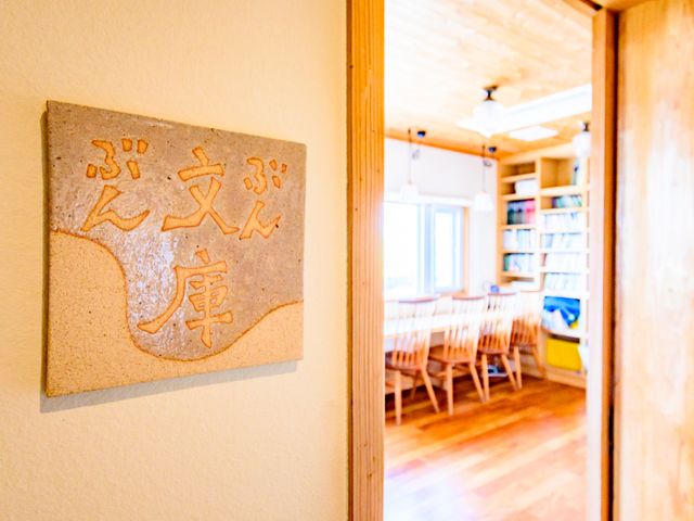 温かみのある居室入口 共有スペース 温もりを感じる空間の入口に設置された、心地よい印象を与える看板です。そこから垣間見える広々とした読書スペースが、心を落ち着かせる時間を提供しています。