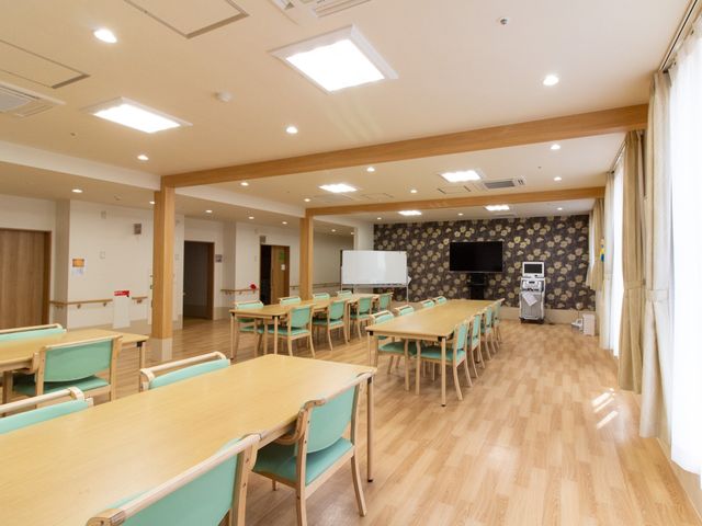 広々とした共有スペース リビングダイニング 天井の高い、ゆったりした食堂で、明るく温もりのあるデザインです。テーブルや椅子も広く配置され、共に時を過ごせる心地よい空間となっています。