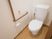 白い壁に木目調の床が使われたトイレである。壁にはL字型の手すりや、緊急時に連絡するためのボタンが設置されている。