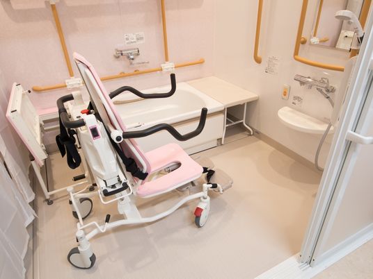 浴室の洗い場に浴室用の車椅子が置かれている。手すりが上下に稼動するようになっている。壁に手すりが取りつけられている。
