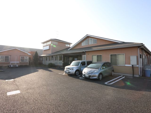 広々とした駐車場のある建物 駐車場 ゆったりとした敷地に佇む、落ち着いた色調の建物です。明るい日差しを浴びて、温かみのある雰囲気が漂います。