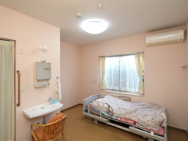 ピンク色の壁の居室 居室 ゆったりとしたベッドが置かれた居室です。日当たりのよい窓や、必要な設備が整った快適な空間となっております。