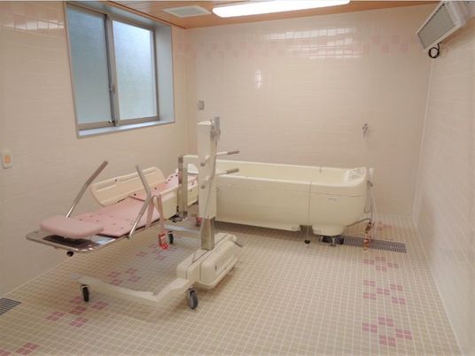 白いタイルで統一された浴室には、ピンク色の機械浴槽が置かれている。