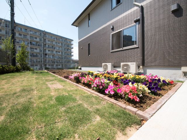 彩り豊かな花壇と建物 花壇 キレイに整えられた花壇が印象的なこのスペースは、穏やかに時間を過ごすのに適しています。