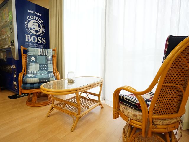 籐製の椅子と自動販売機 共有スペース 籐製の家具が配置された休憩スペースです。手軽に飲み物を選べる自動販売機が設置してあり、一息つく時間を提供しています。