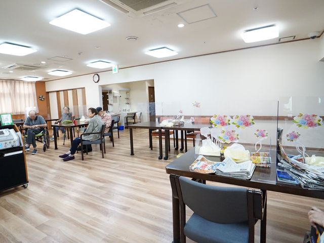 共有ダイニングの様子 居間 明るいダイニングルームで、利用者がくつろぎながら談笑しています。余裕を持ったスペースが、日々の食事や交流を心地よい時間にしています。