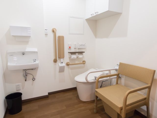 バリアフリー設計のトイレ トイレ 安心してご使用いただける手すり付きの清潔なトイレ空間です。座りやすい椅子も設置され、快適さを追求しています。