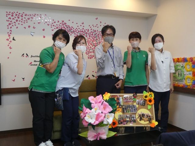 スタッフ集合のラウンジ ラウンジ   装飾された明るいラウンジで、スタッフの皆さんがそろって笑顔のポーズをしています。季節感のある掲示や飾りがあり、和やかな雰囲気です。