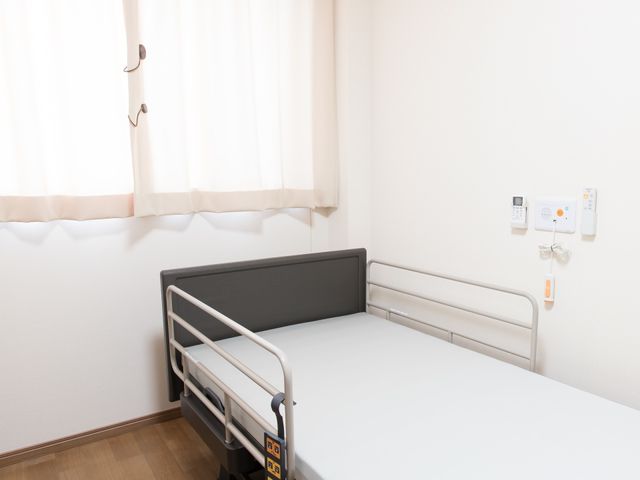 清潔なシングルベッドの居室 介護用ベッド ゆったりとしたシングルベッドが完備された居室です。周辺には必要な備品が整えられ、快適な空間を提供しています。