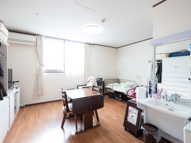 ゆったり居室の風景 部屋 居室には必要なものが整っており、明るい窓辺では穏やかな時間を過ごすことができます。テーブルと椅子も配置され、ゆとりある空間です。