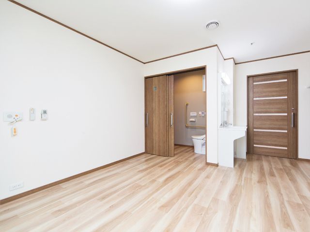 清潔な居室の一部 居室 床と壁の木目が温かみを感じさせる居室です。手すり付きのトイレが併設され、清潔感あふれる住環境が整っています。