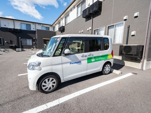 施設の送迎車と外観 施設車 手厚いサポートの象徴とも言える、施設専用の送迎車が停車しており、安心して利用できる環境が整っています。