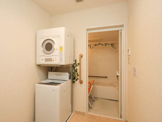洗濯機と浴室の設備 ランドリー 省スペースに設置された洗濯機と扉を開けた浴室という落ち着いた空間です。清潔感があり、自立支援のための工夫もされています。
