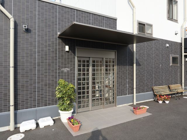 暖かみのあるエントランス 玄関 ゆったりとしたベンチが設置され、植物も飾られた歓迎する雰囲気の入口です。明るい日差しの中で訪問者を迎え入れます。
