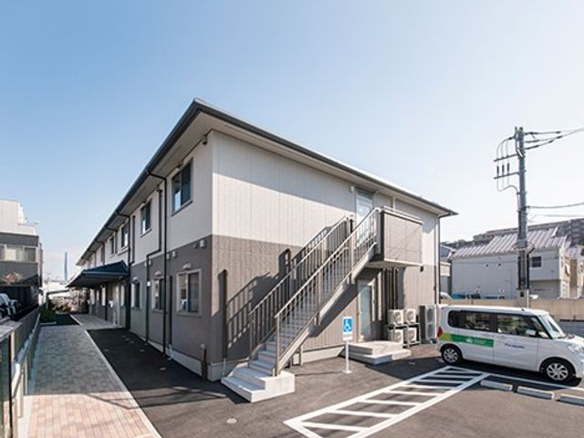 建物外観と駐車場 外観   2階建ての建物の外観で、外階段から上階へ出入りできるつくりです。駐車スペースも見え、送迎時の動線がわかりやすいです。