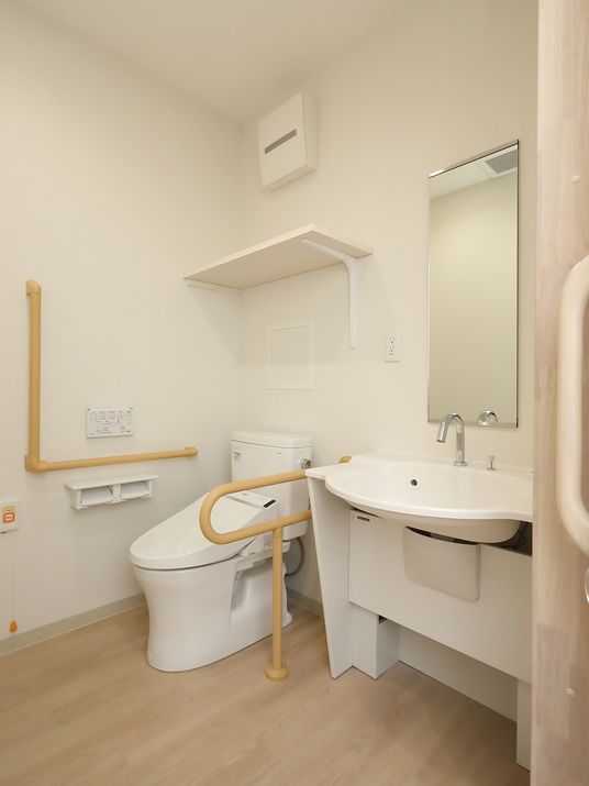 居室には温水洗浄便座のトイレが備わっている。鏡付きの大きな洗面台に手すり、呼出しボタンが設置されている。