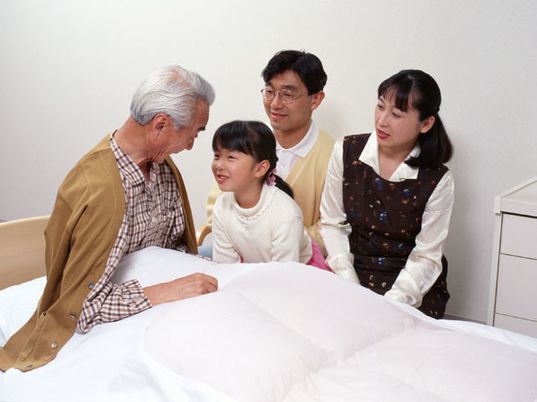 家族と話しながらくつろいでいる高齢者。ベッドの上に座ってリラックスしている