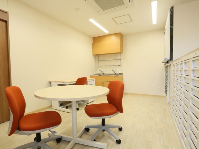 明るい多目的スペース 共有スペース 清潔感のあふれる会議室風の部屋です。赤い椅子がアクセントになっており、打合せや業務に集中できる環境が整っています。