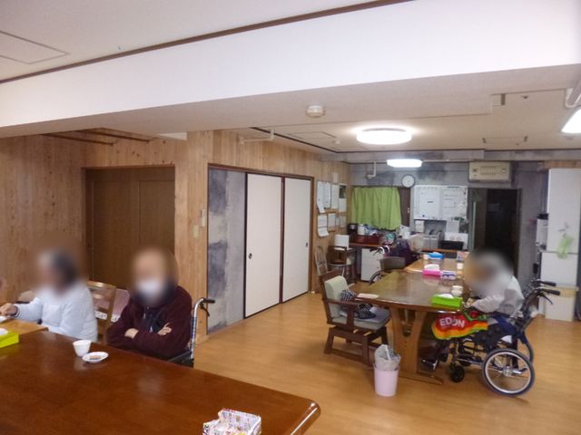 共有エリアの日常風景 2Fデイルーム 暖かみのある木の壁に囲まれた食堂では、利用者が食事や談笑を楽しんでいます。これからの職場として、心地よい環境がお待ちしております。