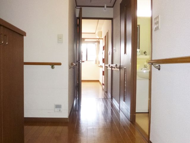 清潔感のある廊下 個室入り口 手すりが整備された広々とした通路は、安全にお過ごしいただける設計です。木目調の落ち着きのあるデザインが魅力的です。
