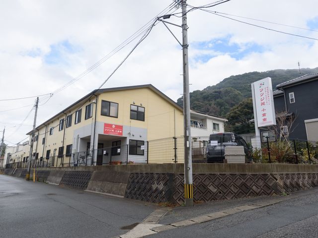 黄色い建物の外観 外観 山々に囲まれた落ち着いた地域に位置する施設です。明るい外壁が周囲からの視認性を高め、訪れる方々を温かく迎えています。
