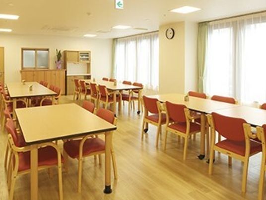 施設の写真 エンジ色の椅子がセットされたダイニングテーブルが並ぶ食堂。奥には食器棚やキッチンがあり、時計も飾られている。