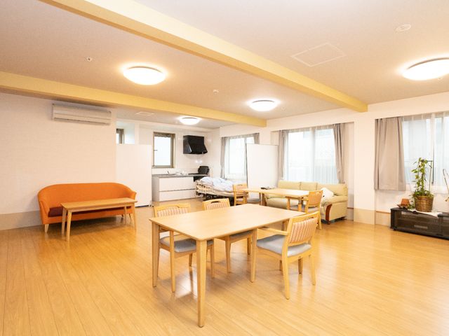 共用リビングの暖かい雰囲気 共有スペース 床の木目が心地よいリビングは、ゆったりとしたソファやテーブルが配置され、穏やかな時間を過ごすことができます。窓からは自然光が差し込み、明るく開放的な空間を提供しています。