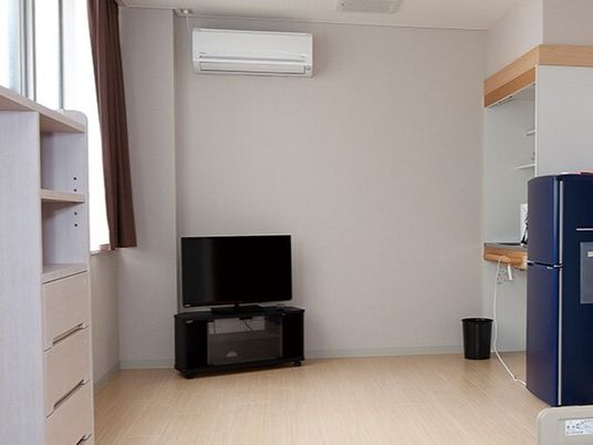 車いす対応のキッチンや冷蔵庫、テレビ、エアコンなどが付いたフローリングの部屋には収納家具もある。