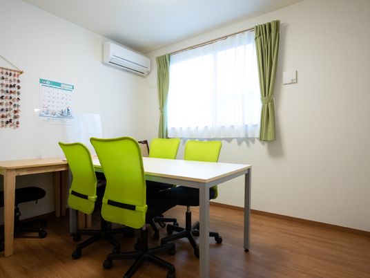 白い机と黄緑の椅子が置かれた白い壁の部屋