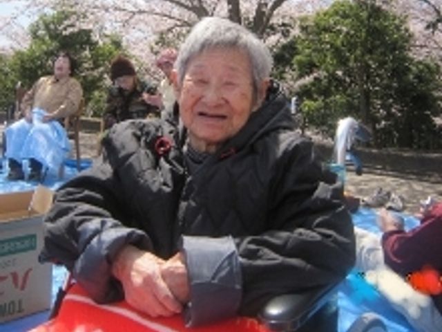 笑顔のご利用者と桜 リハビリ ご高齢の方が、桜を背景に穏やかな表情で過ごされており、屋外でのひと時が楽しめる環境が整っています。