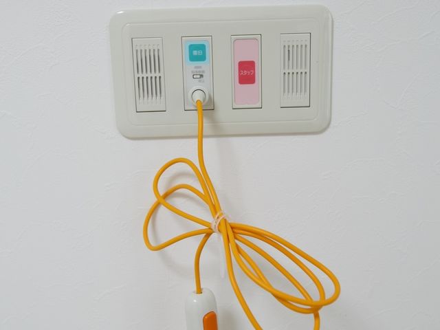 白壁に取り付けられたナースコール 居室 常に利用者の安全を考えた設備が整っており、ナースコールによる迅速な対応が可能です。安心して就業できる環境がここにあります。