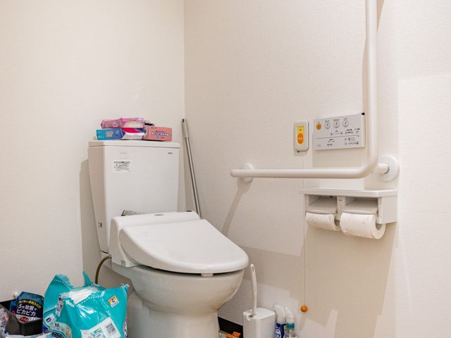 手すり付きトイレ トイレ   手すりが設置された使いやすいトイレです。床は木目調で、清掃用品も整えられています。
