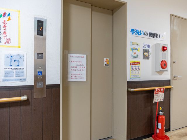 エレベーター前の廊下 廊下   木目調の床と手すりがある落ち着いた廊下です。エレベーター前には案内や安全設備が整っています。